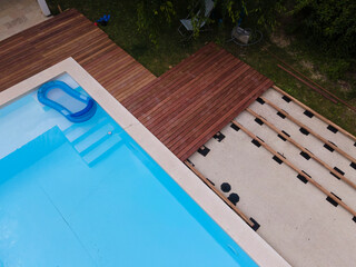 Drone flight over beautiful green garden with pool and the wooden terrace of the pool is currently in progress