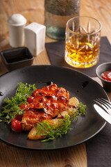 culinary dish chicken steak. restaurant serving. black tableware, wooden table