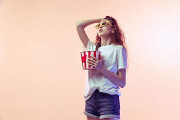 Portrait of young emotive girl in casual outfit posing with popcorn basket isolated over pink...