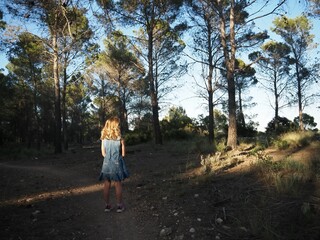 Niña en bosque esperando sola y mirando rayos de luz al atardecer