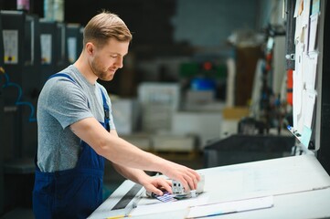 Man worker measuring printing color with spectrometer on the operating desk of the printing plant