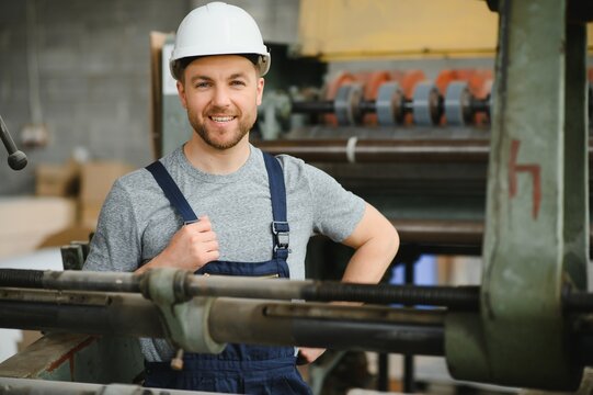 Smiling and happy employee. Industrial worker indoors in factory. Young technician with white hard hat.
