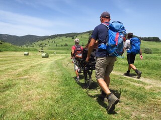 Randonnée en montagne solidaire avec handicapé en joelette fauteuil roulant de randonnée sur les sentiers avec des gens et personne en handicap