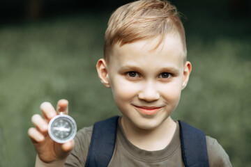 Caucasian cute kid boy with a backpack travels with a compass. Child boy scout holding in a hand...