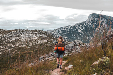Man hiking towards Valley on a trail with a brown hiking backpack and orange tent on his back In the Witfontein nature reserve in Western cape