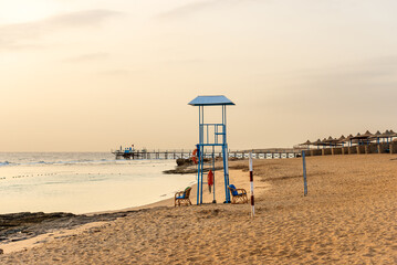 Empty sandy beach near Marsa Alam in the morning with a wooden pier above the coral reef used for diving, snorkeling and swimming and a group of beach umbrellas. Egypt, Africa.