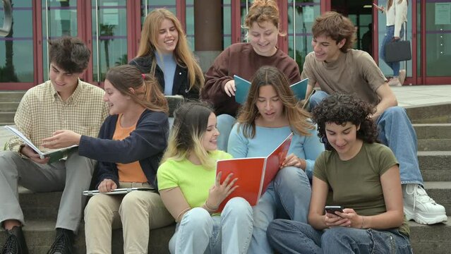 Group of happy multiethnic students reading notes near university building