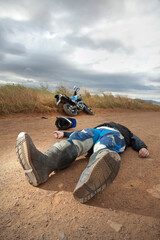 A motorcyclist lying on a dirt road after what seems like an accident.