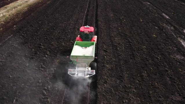 Tractor spreads dry mineral fertilizers on a field of farmland of winter or spring grain crops. Seasonal increase in germination and crop yield.