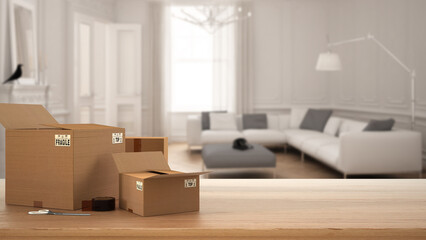 Wooden table, desk or shelf with stack of cardboard boxes over blurred view of classic living room with large sofa, modern interior design, moving house concept with copy space