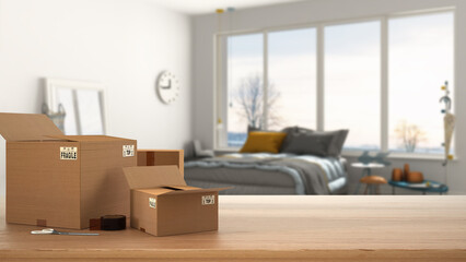 Wooden table, desk or shelf with stack of cardboard boxes over blurred view of colored bedroom with bed and window, modern interior design, moving house concept with copy space