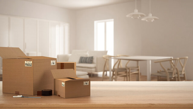 Wooden table, desk or shelf with stack of cardboard boxes over blurred view of dining and living room with soda and table, modern interior design, moving house concept with copy space