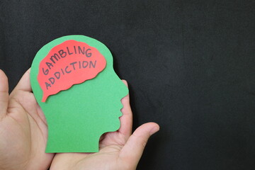Gambling addiction treatment, rehabilitation psychotherapy, and how to deal with concept. Hand holding human head profile with addiction word on brain.