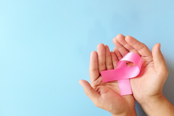 Top view of hand holding color pink awareness ribbon. Women's health and breast cancer awareness care and prevention concept.