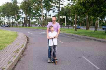 Cute boy in a white T-shirt rides with his dad on a scooter