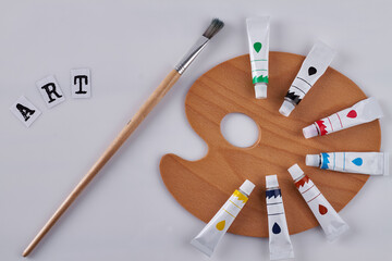 Paint brush and clean wooden palette on white background. Paintbrush for oil painting and colored tubes. Top view art concept.
