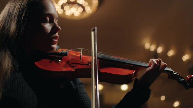 symphonic orchestra in opera house, female violinist is playing classic music in dark philharmonic hall