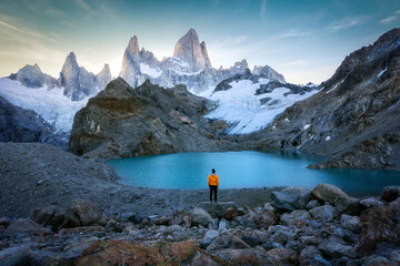 Anonymous traveler admiring alpine lake surrounded by rocky cliffs