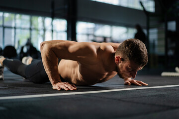 Fototapeta premium Man doing push ups in a gym. Exhaling and inhaling after push-ups and exercise. Perfect for fitness and workout. Young sports man performs pushups in the gym. The athlete is engaged in fitness