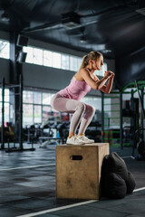 Fit female athlete jumping box at body training in dark gym. Fitness woman jump exercise in sport...