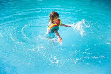 Kind mit Schwimmflügel planscht im hellblauen Pool. Child with water wings splashes in the light...