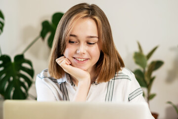 Young smiling woman having video call on laptop at home. Girl greeting friends on a video chat. Female entrepreneur working on laptop at home office. Remote work concept. A business woman is