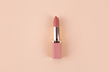 nude matte lipstick on a beige background in a pink and gold tube top view, flatlay. Professional cosmetic product for the work of a makeup artist flat lay. Bright backdrop vertical - obrazy, fototapety, plakaty