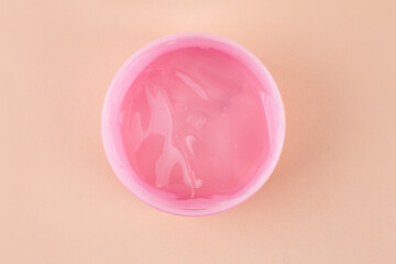 Pink jar of transparent cosmetic gel on beige background, closeup. Cosmetology and beauty concept