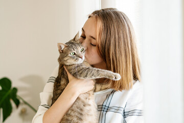 Indoor shot of amazing lady holding pet. Portrait of young woman holding cute striped cat with green eyes. Female hugging her cute kitty. Adorable domestic pet concept. Indoor shot of amazing lady