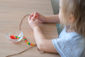 small child, toddler stringing colored plastic beads on string, kid's fingers close-up, concept of...