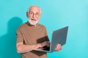 Portrait of attractive cheery grey-haired man holding in hands using laptop isolated over bright blue color background