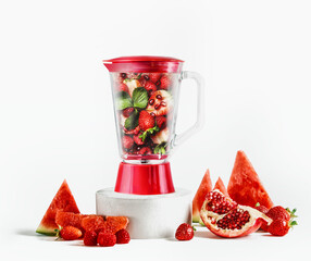 Glass blender filled with red fruits: watermelon slices, pomegranate seeds, raspberries,...