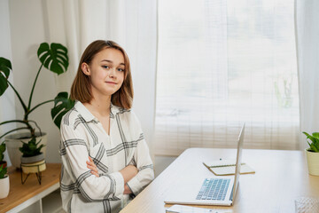 Young woman entrepreneur working on laptop at home. Girl using a computer for study online at home, female user busy on a distance internet job. Cozy office workplace, remote work, e-learning concept