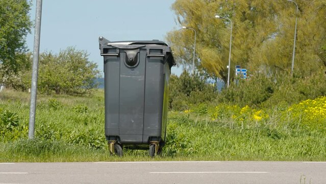 A black garbage bin on the side of the pole in Estonia on a bright sunny day