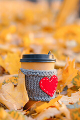 Paper coffee cozy cup with heart shape in autumn leaves, vertical copy space