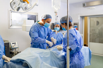 Fototapeta Group of medical team urgently doing surgical operation and helping patient in theater at hospital. Medical team performing surgical operation in a bright modern operating room obraz
