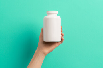 Female hand holding white bottle of medication pills  or vitamins or supplements