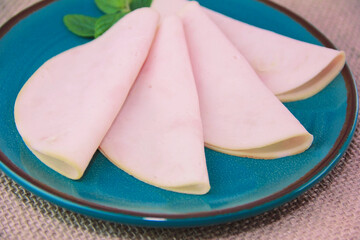 round thinly sliced pieces of meat sausage ham on a blue plate