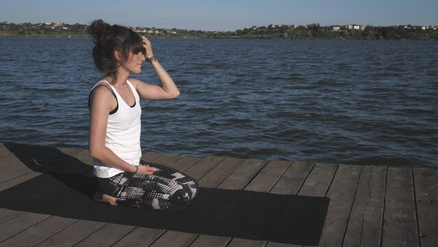 a young woman practices yoga on a pier by the lake. A woman in black leggings practices yoga. slow motion 4K