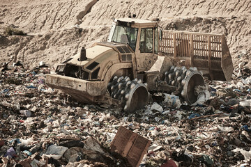 Fototapeta premium Heavy machinery shredding garbage in an open air landfill. Pollution