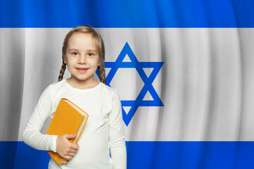 Pretty little kid girl holding book against Israeli flag background