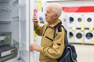 elderly man choosing refrigerator in showroom of electrical appliance store
