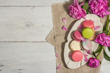 Obraz na płótnie Canvas Macarons with a bouquet of peonies on white wooden background. Sweet dessert, pastel colors