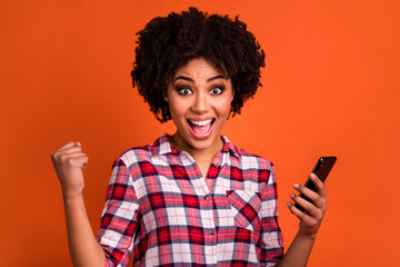 Portrait of delighted person raise fist celebrate follow hold phone isolated on orange color background