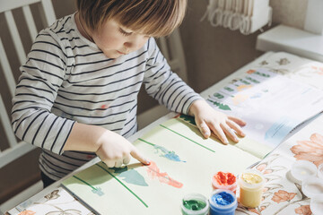 Finger painting. Portrait of cute little boy painting with fingers at home. Close-up of child's hand in colorful paints. Early education concept. Sensory play. Development of fine motor skills.