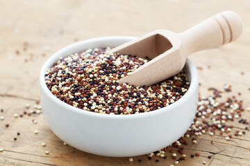 Quinoa in white bowl with scoop on wooden table