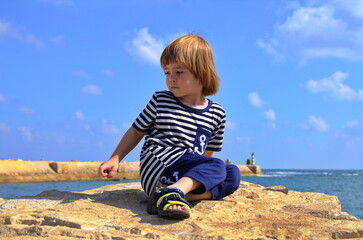 A boy in a vest looks at the sea, ocean. Children in yacht marina. Active vacation with kid. Holiday activity with child. Family water fun. Kid on stripes t-shirt. Concept: sailing, yachting, travel