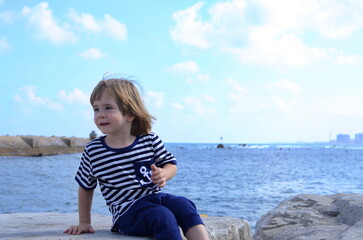 A boy in a vest looks at the sea, ocean. Children in yacht marina. Active vacation with kid. Holiday activity with child. Family water fun. Kid on stripes t-shirt. Concept: sailing, yachting, travel