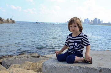 Naklejka na ściany i meble A boy in a vest looks at the sea, ocean. Children in yacht marina. Active vacation with kid. Holiday activity with child. Family water fun. Kid on stripes t-shirt. Concept: sailing, yachting, travel