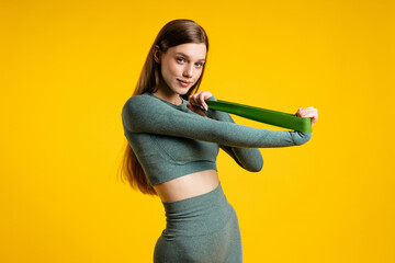 Sports girl with a rubber band for fitness on a yellow background